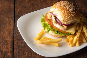 Hamburger and French fries placed on a white plate on rustic wood with black background, selective focus.