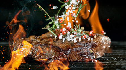 Tasty beef steak on cast iron grate with fire flames. Freeze motion barbecue concept.