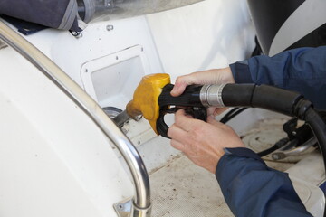 Hands with yellow fuel gun in motor boat fuel filler socket on gas station, watercraft refueling on...