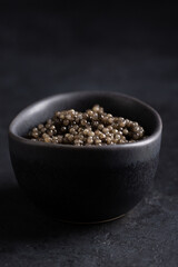 Sturgeon black caviar in black bowl on black background. Copy space. Close-up.