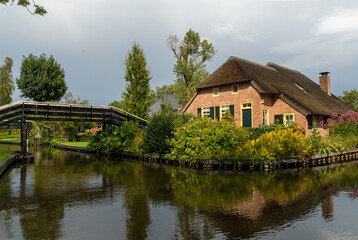 Giethoorn, The Netherlands - August 28, 2020: Red thatched-roof house behind the wooden bridge