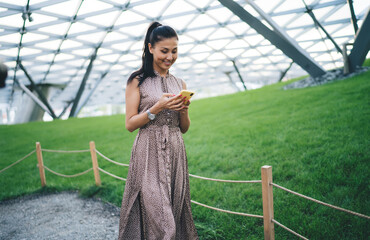 Asian youngster woman spending leisure in conservatory greenhouse creating web content for sharing information about leisure in orangery, happy millennial connecting to mobile internet for messaging