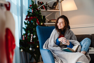 Photo of girl drinking coffee and reading book while sitting on armchair