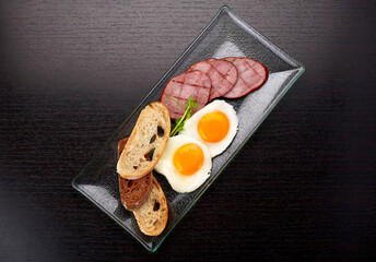 Fried fried eggs with tomatoes, ham and ciabatta toast, on a dark background. Breakfast
