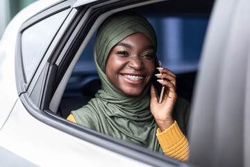 Black muslim woman traveling on car back seat and talking on cellphone