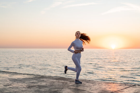 Image of redhead sportswoman running while working out on promenade