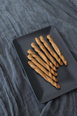 Delicious bread sticks standing on black plate, grey background