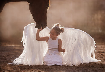 Beautiful blonde child girl in the image of an angel with a horse
