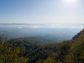 Scenic view from Kozara mountain to the valley filled with fog and smoke during a sunny day.