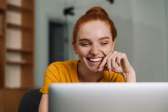 Image of laughing beautiful redhead girl using laptop while working