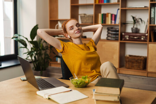 Image of relaxed redhead girl using earphones while working with laptop