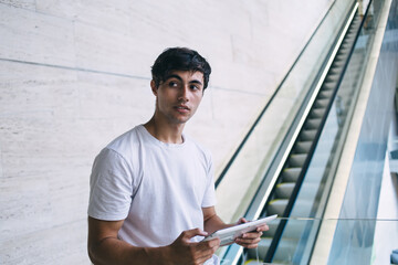 Thoughtful caucasian millennial hipster guy holding modern digital tablet searching information and browsing, serious young 20s male playing online games via touchpad on free time indoors