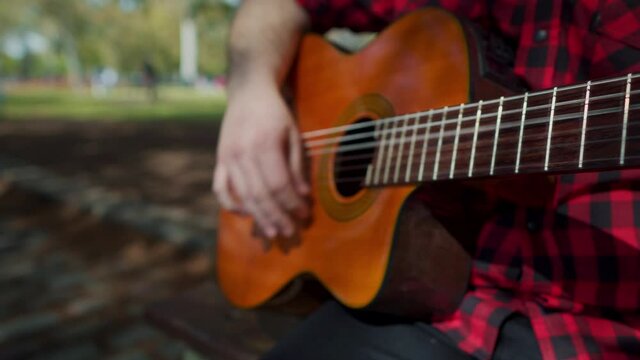 Close up shot of the hands of a man playing guitar at park. Dolly in