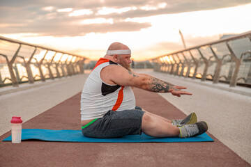 Fat caucasian bearded and bold man with tattoos is doing morning exercses to loose his weight