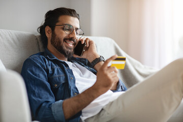 Online Banking. Handsome Western Guy Using Cellphone And Credit Card At Home