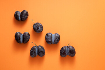 Ripe ugly plums. Fused prunes on a orange background. Space for text. Concept - reduction in vegetable or food waste