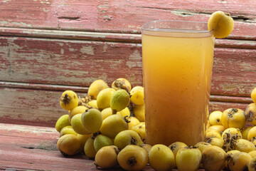 Yellow medlar juice on aged red wooden background