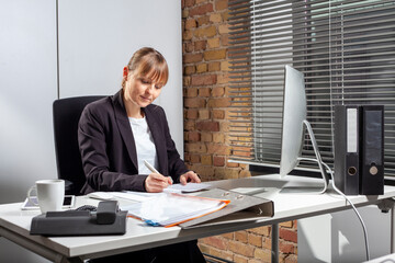 Young ambitious woman sits at her desk and checks important documents in preparation for the next meeting