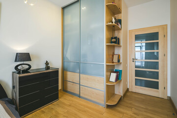 Modern interior of luxury bedroom. Stylish dark dresser. Glass sliding door wardrobe with wooden shelves. Home decor.