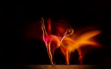 Fireball. Young flexible girl isolated on black studio background in mixed light. Female rhythmic gymnastics artist practicing in action. Exercises for flexibility, balance. Grace in motion, sport.