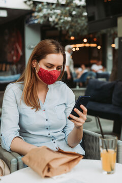 Young Woman With Mask Looking At He Phone, Outdoors In Coffee Shop On Lunch Brake