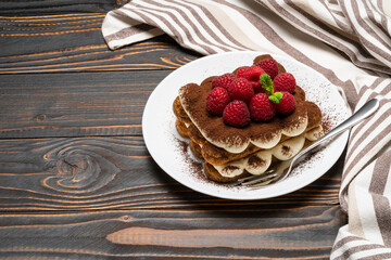 portion of Classic tiramisu dessert with raspberries on ceramic plate isolated on wooden background