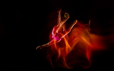 Fireball. Young flexible girl isolated on black studio background in mixed light. Female rhythmic...