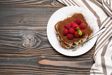 portion of Classic tiramisu dessert with raspberries on ceramic plate isolated on wooden background