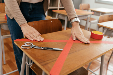 Female teacher using a red tape on the desks in classroom in primary school to keep social distancing measure policy in education building for Covid19 new normal concept.