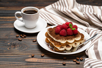 portion of Classic tiramisu dessert with raspberries and cup of espresso coffee isolated on wooden background