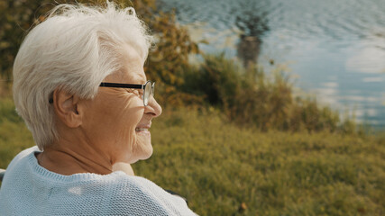 Close up, senior gray haired woman in the wheelchair enjoying autumn breeze near the river. High...