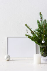 Christmas poster mock up with horizontal frame, fir tree branches in a vase and balls with candles on white wall background, new year and christmas concept