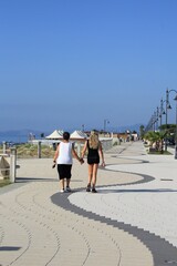 Mother and daughter walk along the promenade of Ardore in Calabria. Walking by holding hands. Two women filmed from behind as they walk. Two people on the seafront. Original corrugated flooring - wave