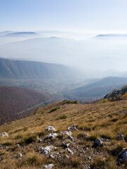 Scenic view from Vlašić mountain to the valley filled with fog and mountain peaks above the fog in autumn during a sunny day