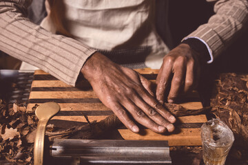 Closeup of men's hands making cigar from tobacco leaves. Traditional manufacture of cigars..Demonstration of production of handmade cigars. Hands rolling dried and cured tobacco leaves.