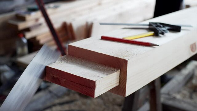 Close view of unidentified carpenter cutting a wooden plank with a small manual saw. Carpenter workshop
