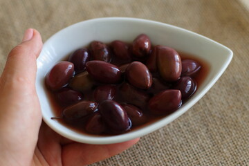 Olives kalamata on white plate with dark marinade. Special Greece receipt of olives. 