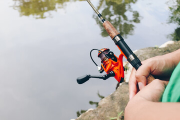 Close up of spinning with the fishing reel in the hand, fishing hook on the line with the bait in the left hand against the background of the water.