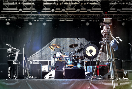 Empty illuminated stage with drum kit, microphones and film camera