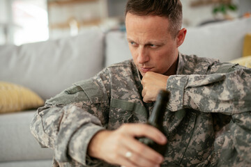 Depressed soldier with bottle sitting in livig room., Alcohol addiction...