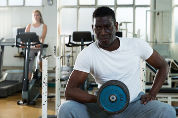 Fototapeta na wymiar Portrait of African man doing exercises with dumbell at gym