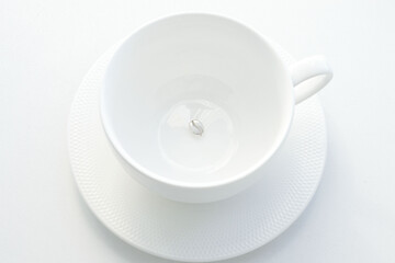 pendant made of silver in the form of a coffee bean, at the bottom of a white porcelain mug, on a white background. Jewelry, pendant for coffee lovers. Memorable gift, relationship, love. Coffee day.