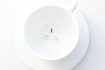 silver pendants in the form of coffee beans, at the bottom of a white porcelain mug, on a white background. Jewelry, pendant for coffee lovers. Memorable gift, relationship, love. Coffee day.
