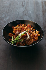 Beautiful chickpea appetizer in black plate on wooden background. European cuisine, dish from menu, vegetable snack. Vertical photo.