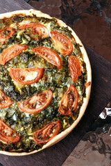 Pie with spinach and tomatoes lies on table. Homemade pie for the whole company made from vegetables. Vertical photo.