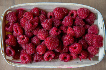
Lots of ripe red raspberries in a white basket