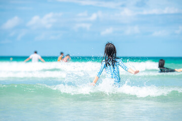 Rear view of Asian child girl jumping in water at the seaside.Relaxing, fun, and enjoy holiday at tropical paradise beach with blue sky, healthy lifestyle concept.