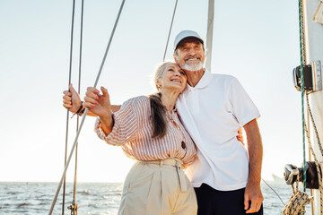 Happy mature couple embracing each other and looking away. Two people standing on sailboat and smiling.
