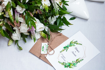 Wedding accessories. Wedding invitation, white shoes and bridal bouquet with white roses on a light background. Text on the invitation: "Pavel and Lilia. July 25, 2020"