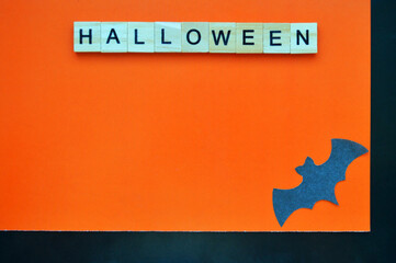 Black paper bat lies on orange-black background. Word halloween of wooden blocks with letters